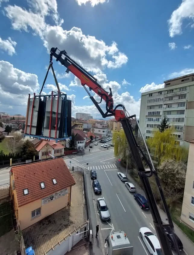Macara care ridică un pachet de dimensiuni mari deasupra unei străzi