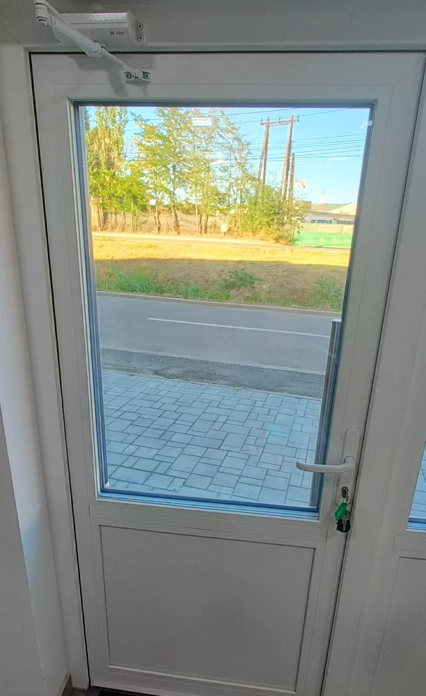Ușă albă cu geam și mâner, văzută din interior, cu o alee pavată în fața ei