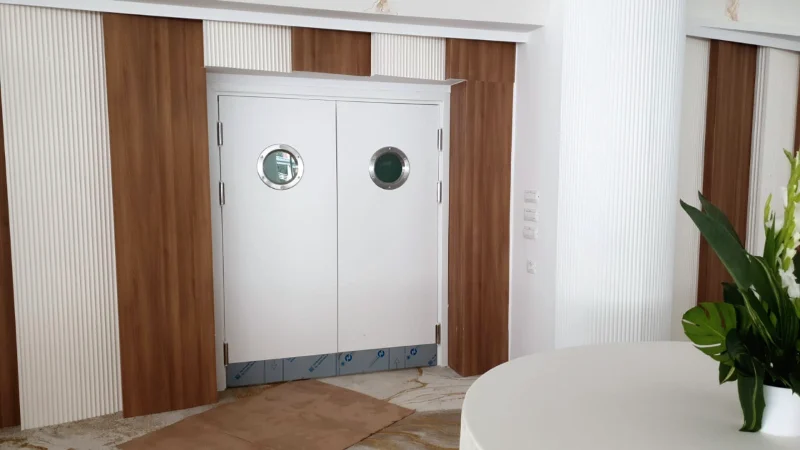 Ușă dublă albă cu hublouri rotunde, într-un perete placat cu lemn și riflaj alb, în timpul lucrărilor