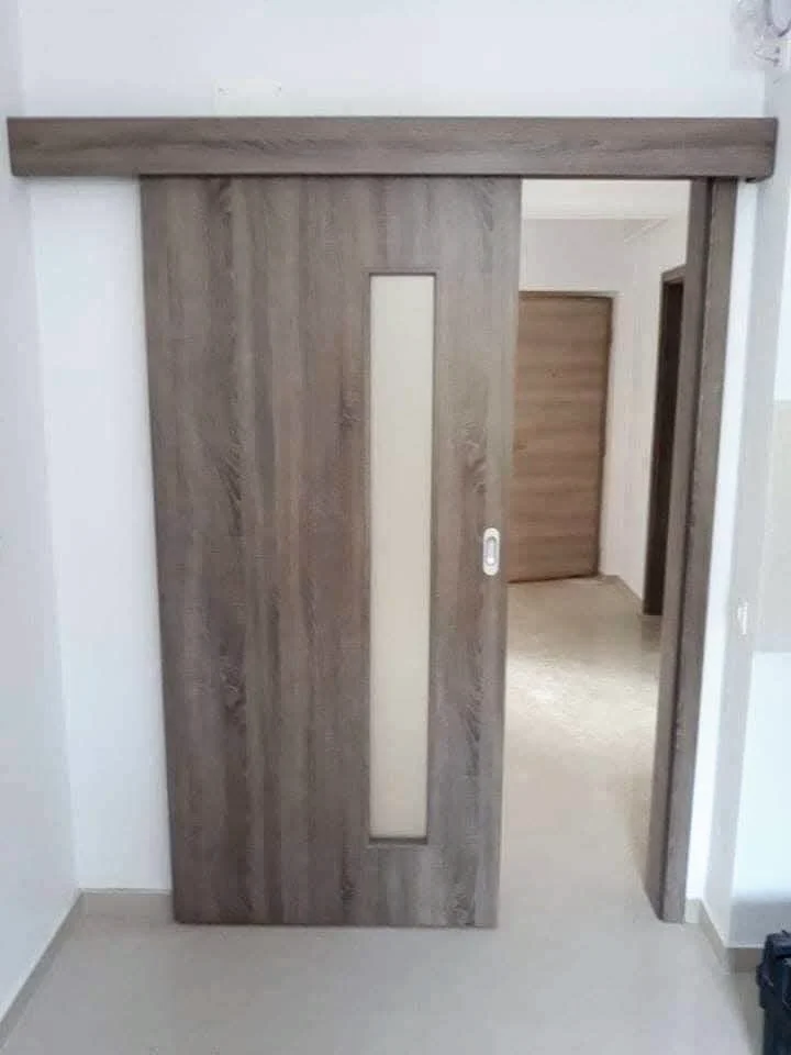 Ușă glisantă în decor lemn cu inserție verticală de sticlă, montată pe perete