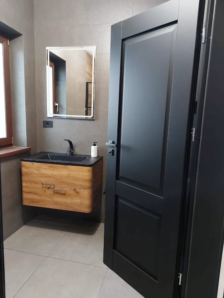 Ușă de interior clasică, neagră, deschisă spre o baie cu mobilier din lemn