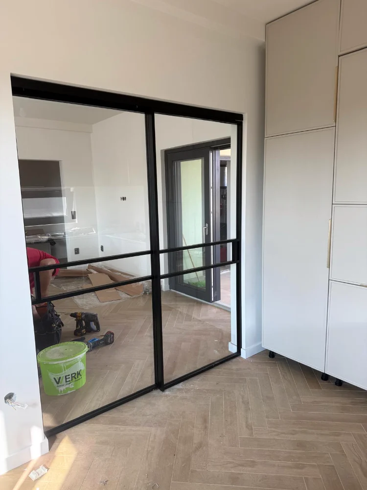 Separeu cu ramă neagră și sticlă într-o încăpere cu parchet în model spic, în timpul lucrărilor